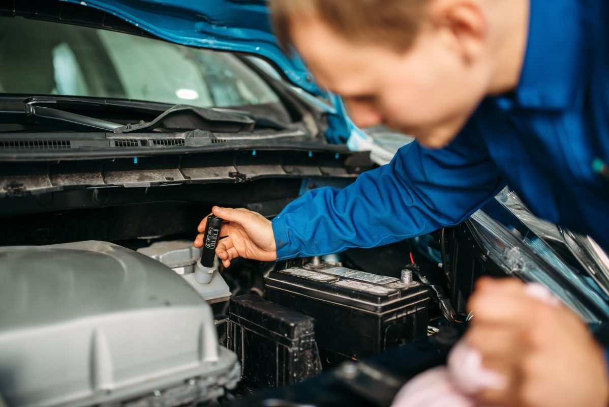 Male technician checks brake fluid level in car. Auto-service, vehicle maintenance, repairman with tools